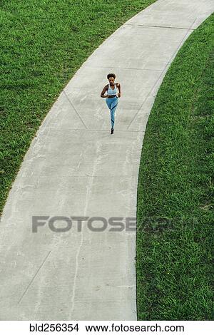 Picture - Distant mixed race woman running on path in park. Fotosearch