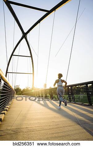 Stock Image - Distant mixed race woman running on bridge. Fotosearch