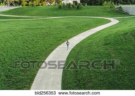 Stock Image - Distant mixed race woman running on winding path in park. Fotosearch