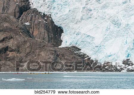 Stock Photo - Distant people kayaking near glacier. Fotosearch