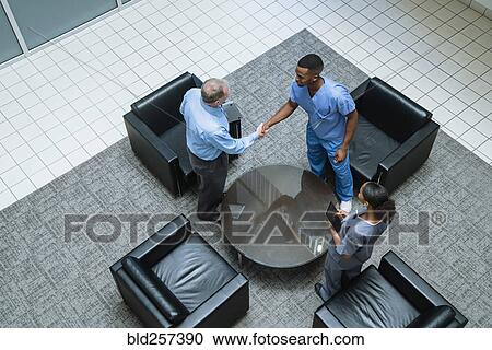 Doctor and nurse shaking hands in lobby View Large Photo Image Stock Image - Doctor and nurse shaking hands in lobby. Fotosearch
