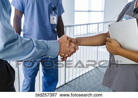 Stock Photo - Doctor and nurse shaking hands near railing. Fotosearch