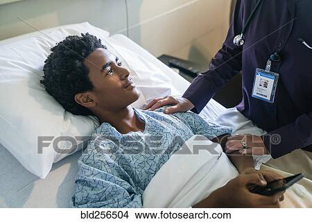 Picture - Doctor comforting boy in hospital bed holding cell phone. Fotosearch