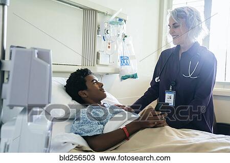 Stock Image - Doctor comforting boy in hospital bed holding cell phone. Fotosearch