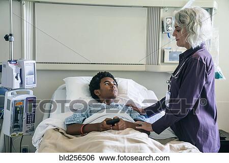 Stock Photograph - Doctor comforting boy in hospital bed holding cell phone. Fotosearch