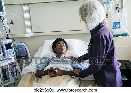 Doctor comforting boy in hospital bed holding cell phone View Large Photo Image Stock Photography - Doctor comforting boy in hospital bed holding cell phone. Fotosearch