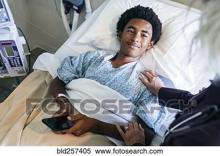 Doctor comforting boy laying in hospital bed holding cell phone View Large Photo Image Stock Photography - Doctor comforting boy laying in hospital bed holding cell phone. Fotosearch