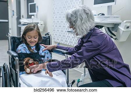 Stock Photograph - Doctor giving teddy bear to girl in wheelchair. Fotosearch