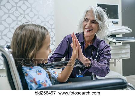 Stock Photo - Doctor high-fiving girl in wheelchair. Fotosearch