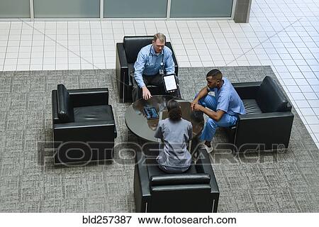Stock Photo - Doctor holding digital tablet talking to nurses in lobby. Fotosearch