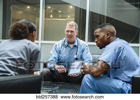 Stock Photo - Doctor holding digital tablet talking to nurses in lobby. Fotosearch