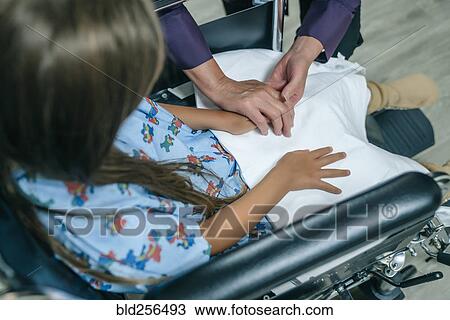 Stock Image - Doctor holding hands with girl in a wheelchair. Fotosearch