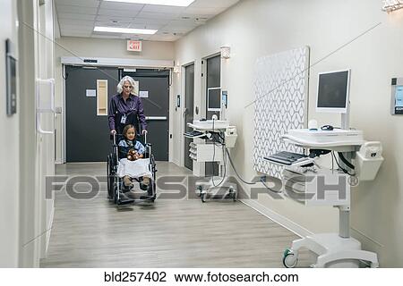 Stock Image - Doctor pushing girl in wheelchair. Fotosearch