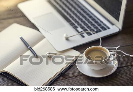 Stock Photograph - Earbuds with notebook and coffee near laptop. Fotosearch