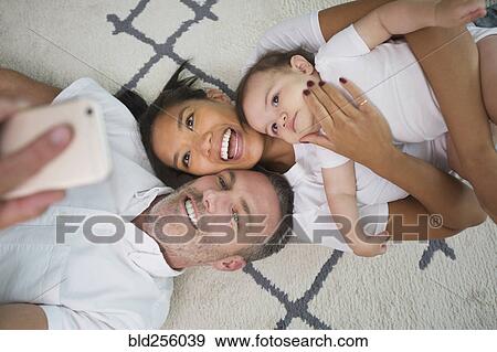 Stock Photo - Family laying on floor posing for cell phone selfie. Fotosearch