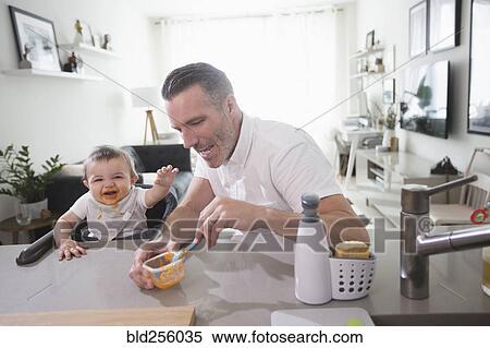 Stock Photography - Father feeding happy baby son. Fotosearch