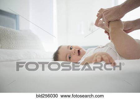 Stock Image - Father holding legs of baby son on bed. Fotosearch