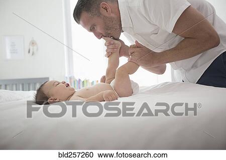 Stock Image - Father kissing feet of baby son on bed. Fotosearch