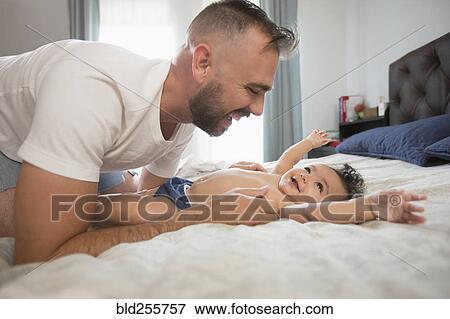 Stock Photo - Father laying on bed playing with baby daughter. Fotosearch