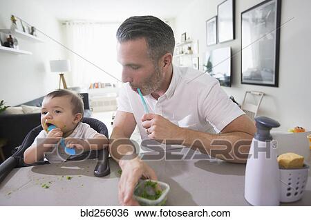 Stock Photograph - Father watching baby son eating. Fotosearch