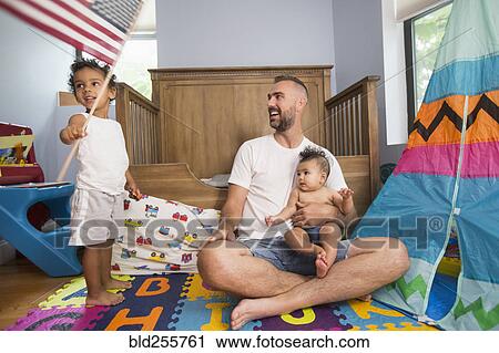 Stock Image - Father watching son waving American flag in playroom. Fotosearch