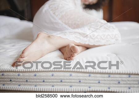 Stock Image - Feet of Caucasian woman laying on bed. Fotosearch