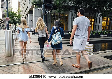 Stock Image - Friends crossing street in city carrying shopping bags. Fotosearch