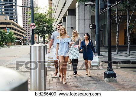 Stock Photo - Friends crossing street in city carrying shopping bags. Fotosearch