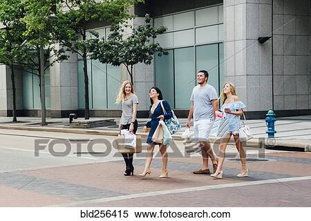 Stock Photography - Friends crossing street in city carrying shopping bags. Fotosearch