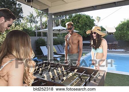 Stock Photo - Friends playing foosball outdoors near swimming pool. Fotosearch