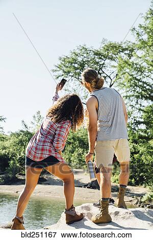 Stock Photo - Friends posing for cell phone selfie on rocks near river. Fotosearch