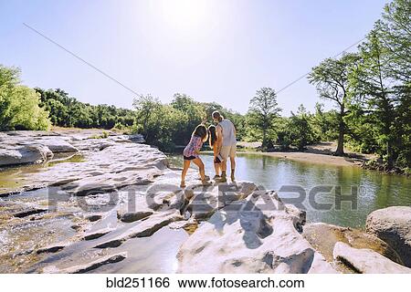 Stock Photograph - Friends posing for cell phone selfie on rocks near river. Fotosearch