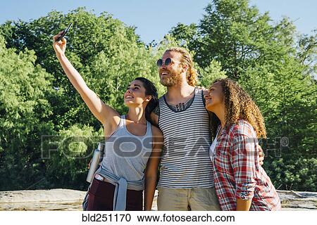 Stock Image - Friends posing for cell phone selfie outdoors. Fotosearch