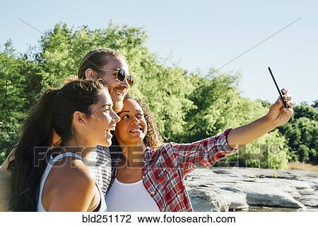 Stock Image - Friends posing for cell phone selfie outdoors. Fotosearch