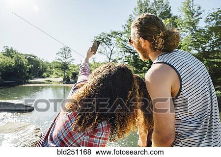 Stock Photo - Friends posing for cell phone selfie near river. Fotosearch