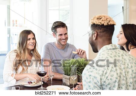 Stock Image - Friends smiling and talking with wine and snacks. Fotosearch