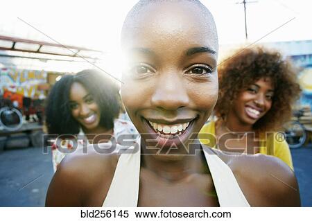 Stock Photography - Friends smiling behind bald woman outdoors. Fotosearch