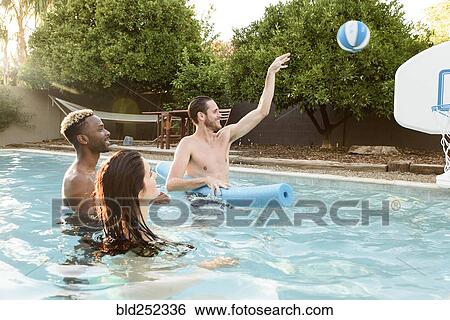 Stock Photograph - Friends watching man shooting basketball in swimming pool. Fotosearch