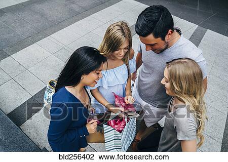 Stock Image - Friends with shopping bags texting on cell phone. Fotosearch