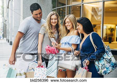 Stock Photograph - Friends with shopping bags texting on cell phone in city. Fotosearch