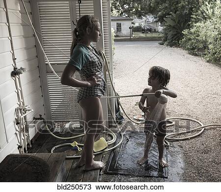 Stock Image - Frustrated Caucasian girl watching brother using shower outdoors. Fotosearch