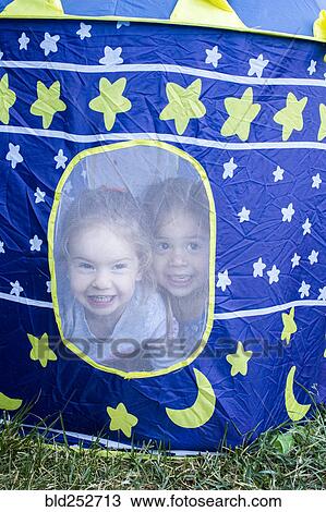 Stock Image - Girls smiling in window of camping tent. Fotosearch