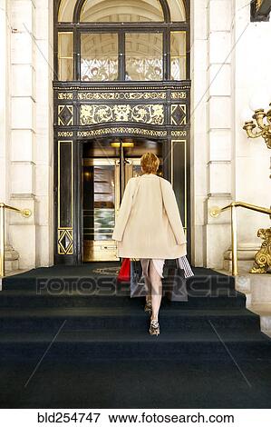 Stock Photo - Glamorous Caucasian woman carrying shopping bags to luxury building. Fotosearch