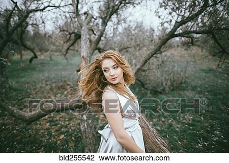 Stock Image - Glamorous Caucasian woman tossing hair near tree. Fotosearch
