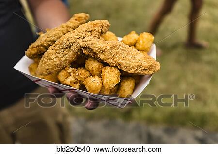 Stock Image - Hand holding container of fried chicken and potatoes. Fotosearch
