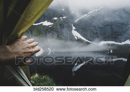 Stock Image - Hand opening tent flap near foggy river. Fotosearch