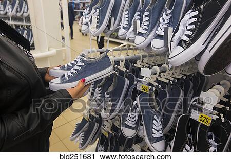 Stock Image - Hands of Caucasian woman holding sneakers in store. Fotosearch