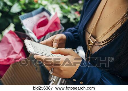 Hands of Hispanic woman with shopping bags texting on cell phone View Large Photo Image Stock Photo - Hands of Hispanic woman with shopping bags texting on cell phone. Fotosearch