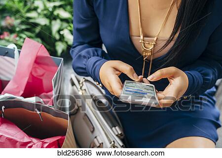 Stock Photograph - Hands of Hispanic woman with shopping bags texting on cell phone. Fotosearch