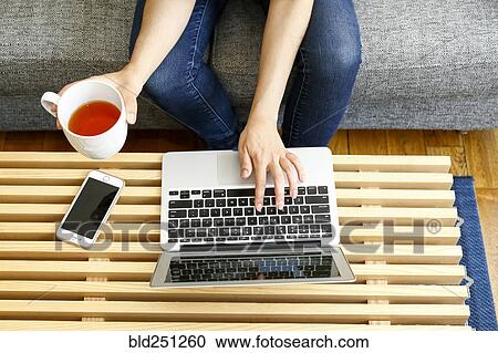 Stock Image - Hands of mixed race woman using laptop and drinking tea. Fotosearch